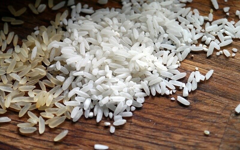 Imagem mostra grãos de arroz integral e arroz branco em cima de uma mesa de madeira; Conab confirma anulação de leilão para importação do grão